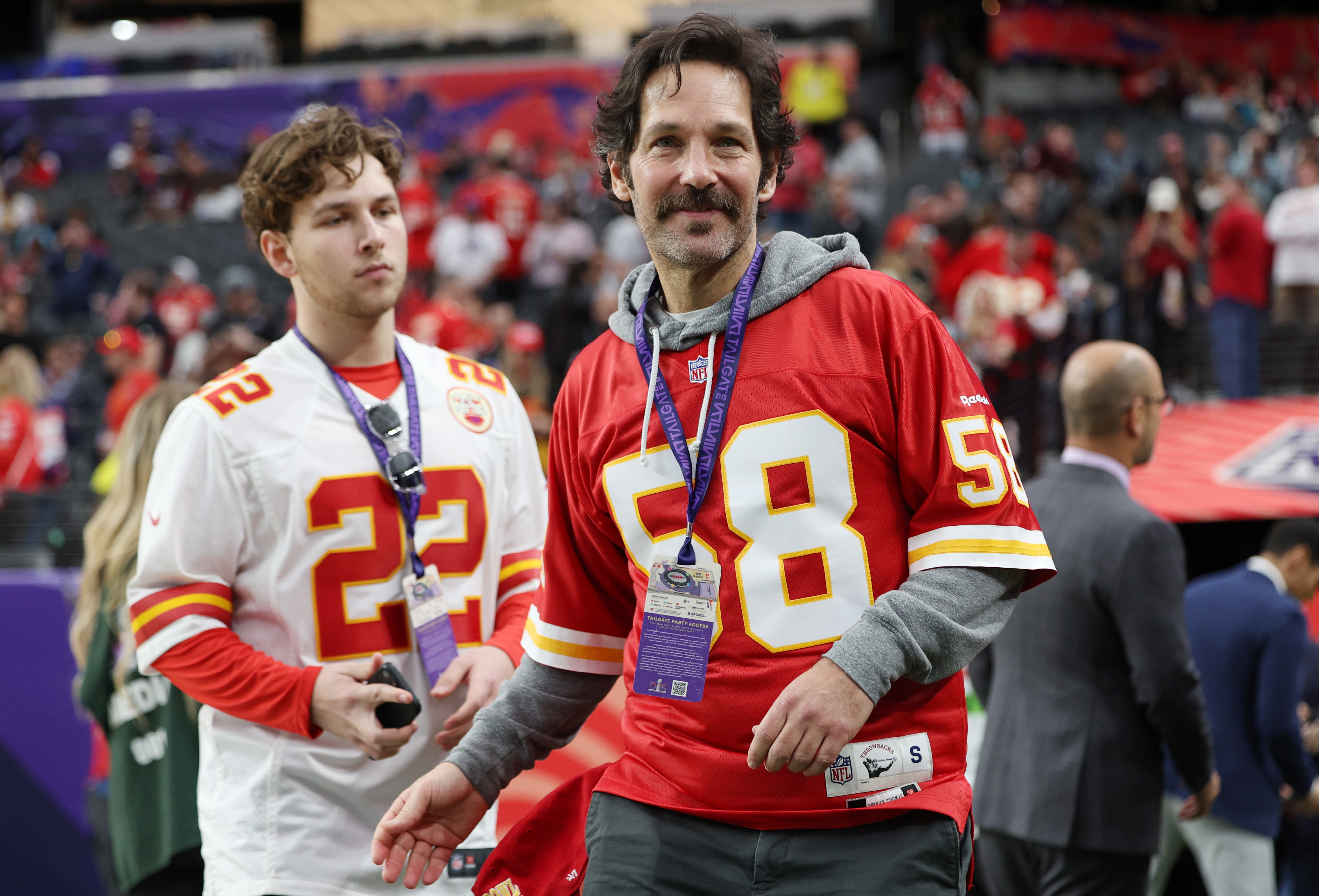 Paul Rudd, in a red Kansas City Chiefs jersey, and Jack Rudd, in a white Chiefs jersey, are standing on a football field