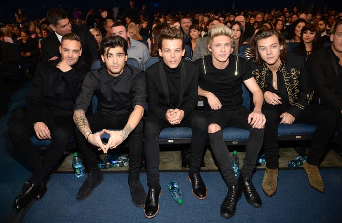 Liam Payne, Zayn Malik, Louis Tomlinson, Niall Horan, and Harry Styles sit in the audience at an event, dressed in stylish dark outfits