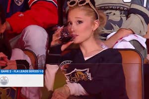 Ariana Grande sits in a hockey arena, sipping a drink and wearing a Florida Panthers jersey. The screen shows "Game 2 - FLA Leads Series 1-0."