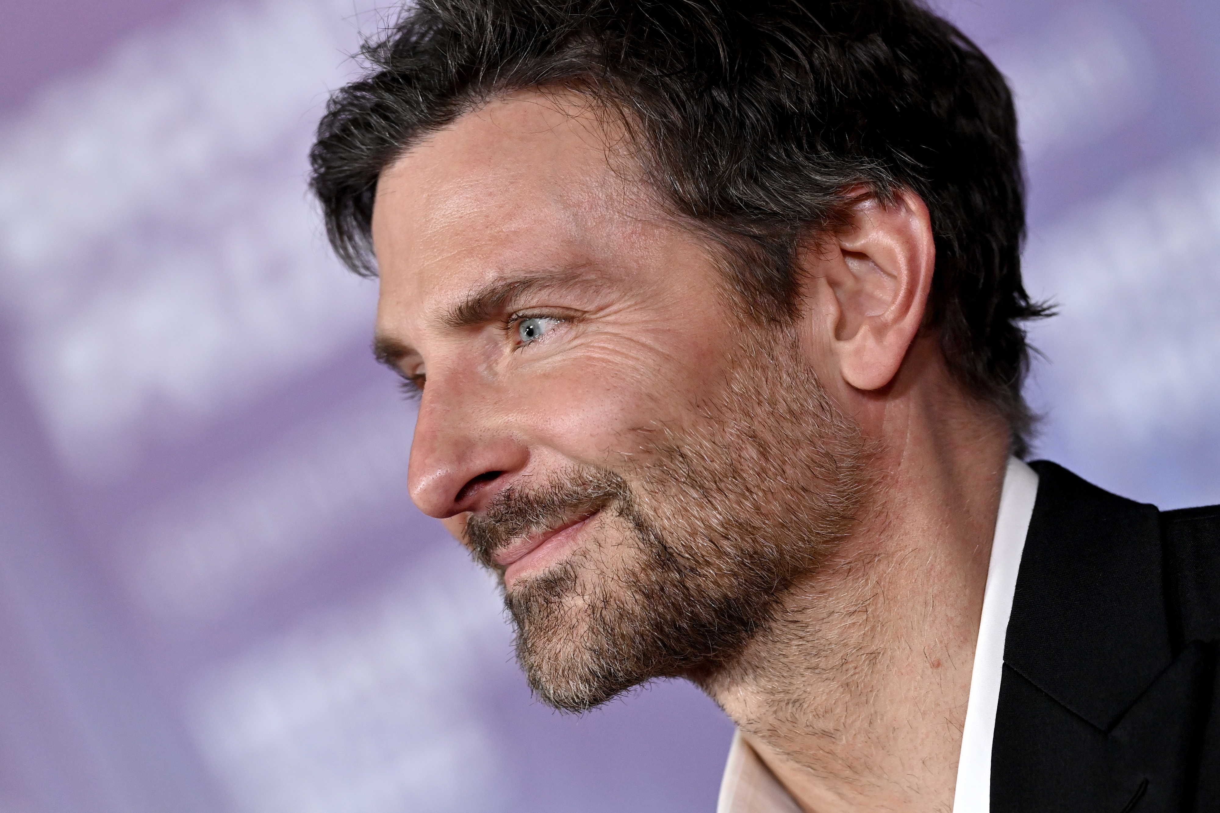 Bradley Cooper in a close-up shot, smiling and wearing a suit at a public event