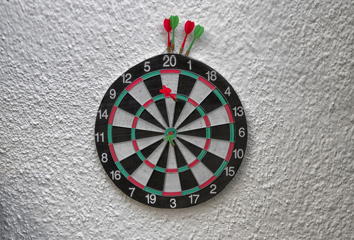 A dartboard with several darts, including one hitting the bullseye, is mounted on a wall