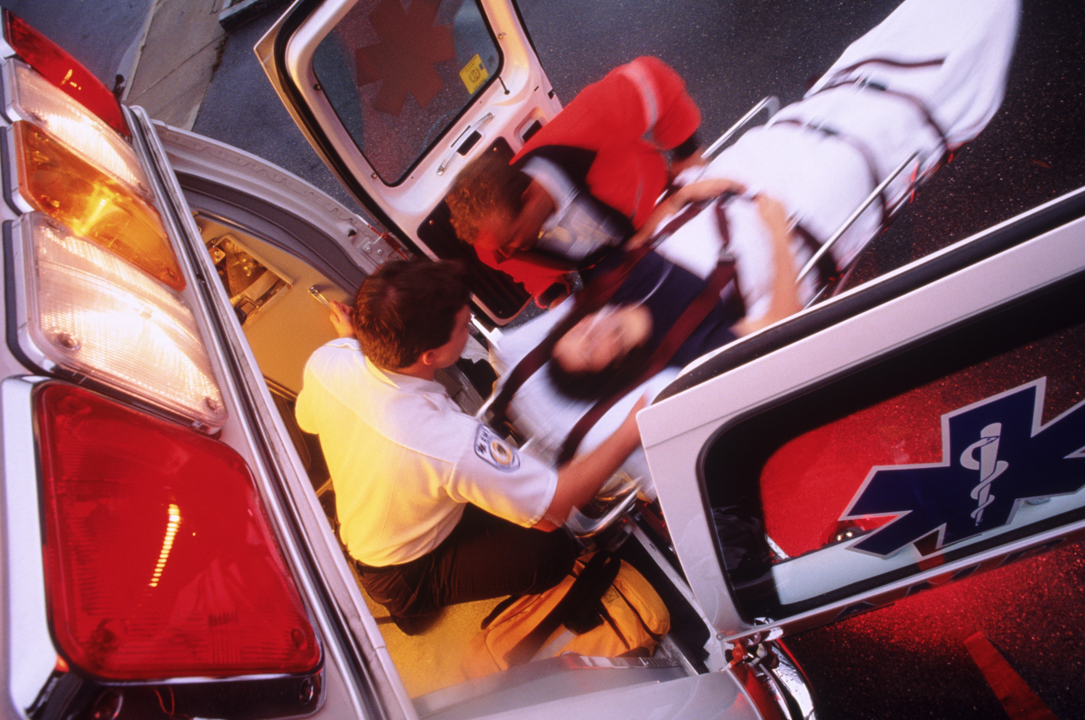 Two paramedics load a person on a stretcher into an ambulance at night