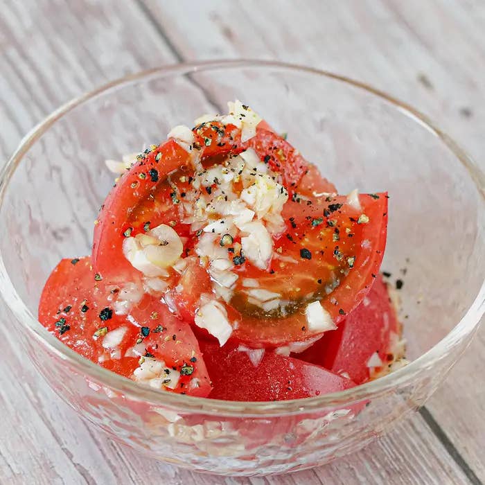 トマトスライスとみじん切りしたニンニクが入ったガラスのボウルに盛られたサラダ。