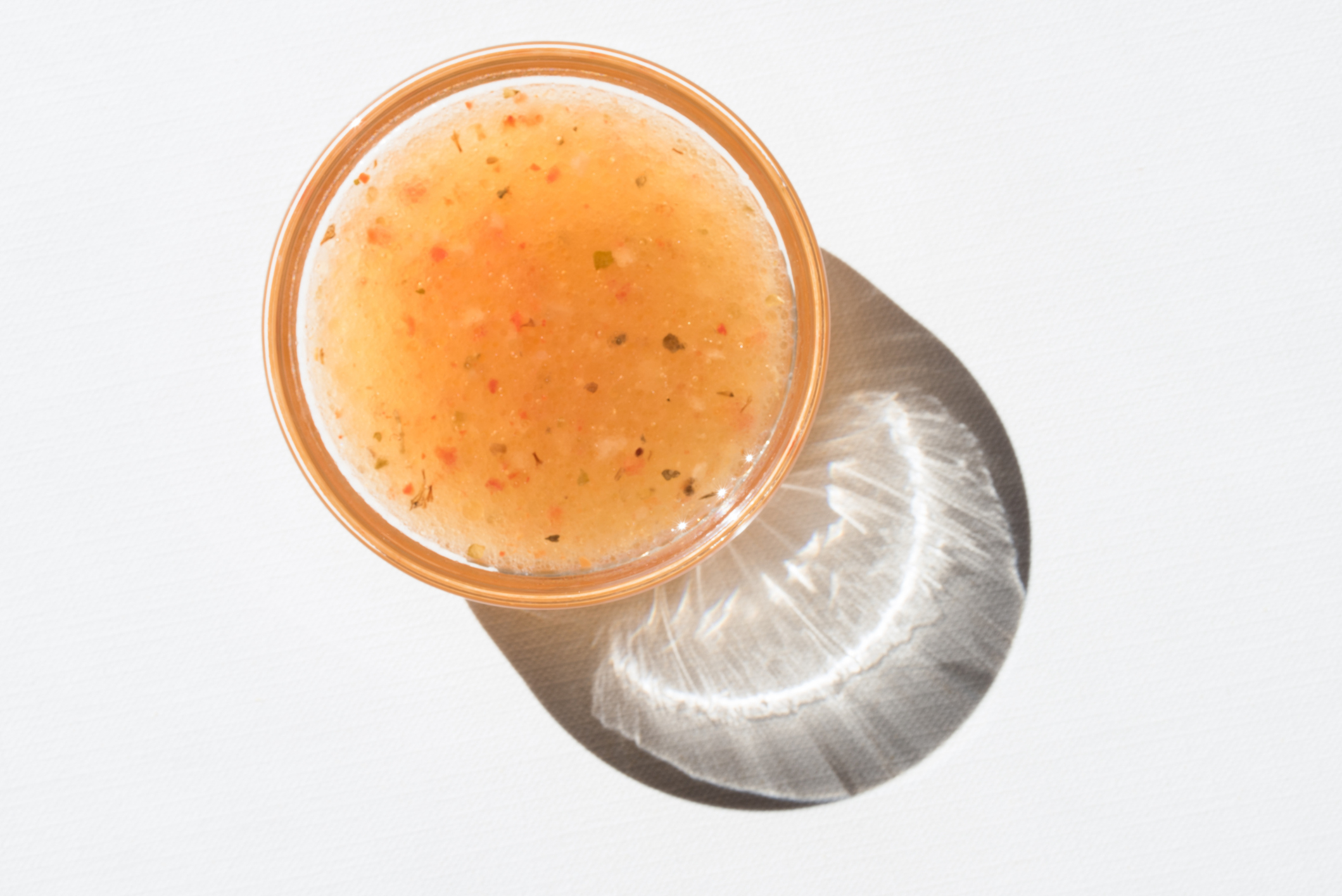 Top view of a bowl of mixed fruit sauce with visible seeds, casting a shadow onto a white background
