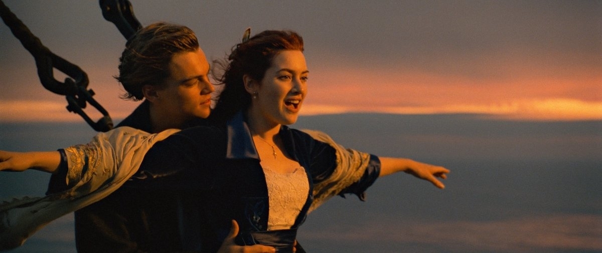 Leonardo DiCaprio and Kate Winslet reenact the famous bow scene from "Titanic," with Kate extending her arms and Leonardo holding her