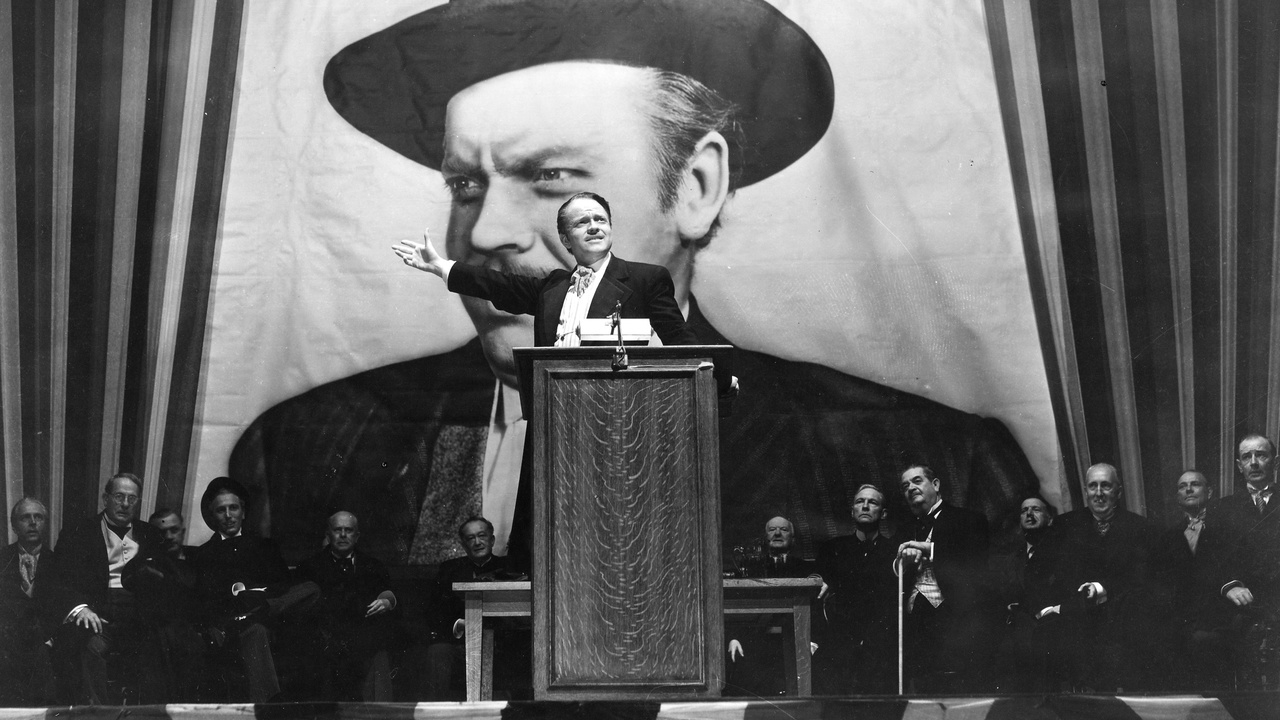 Orson Welles as Charles Foster Kane delivers a speech at a podium with a giant portrait of his character behind him, from the film "Citizen Kane."