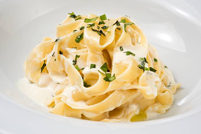 A plate of fettuccine Alfredo garnished with chopped basil