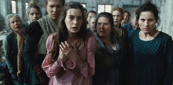 Group of women, including Anne Hathaway, looking anxious in an old, rustic setting, wearing period clothing