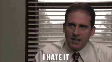 Steve Carell, as Michael Scott from "The Office," is wearing a business shirt and tie and sitting in an office saying, "I hate it."