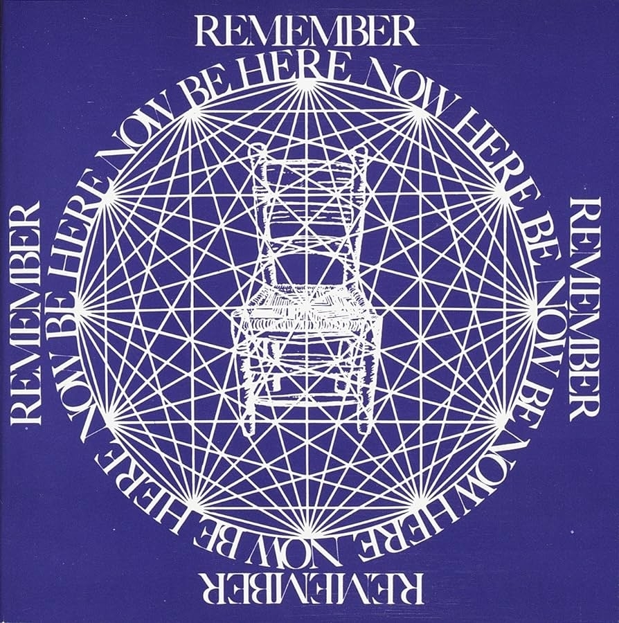 Geometric design featuring a white chair at the center of intertwined circles. Repeating text around the design reads "Remember Be Here Now."