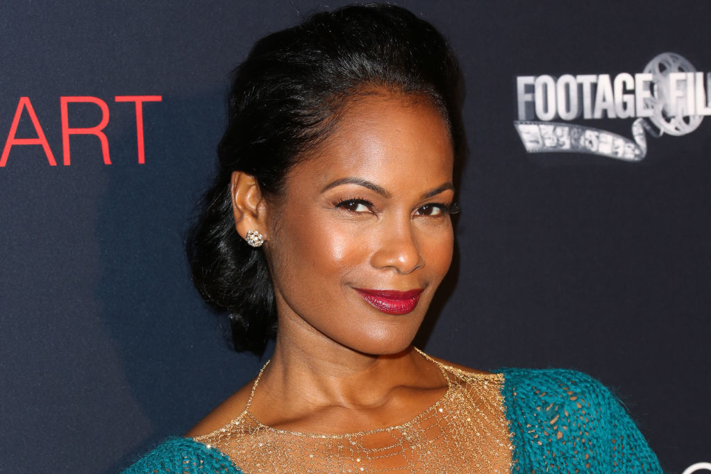 Robinne Lee with a stylish updo hairstyle, wearing an elegant textured top and a gold necklace, posing confidently at a celebrity event backdrop