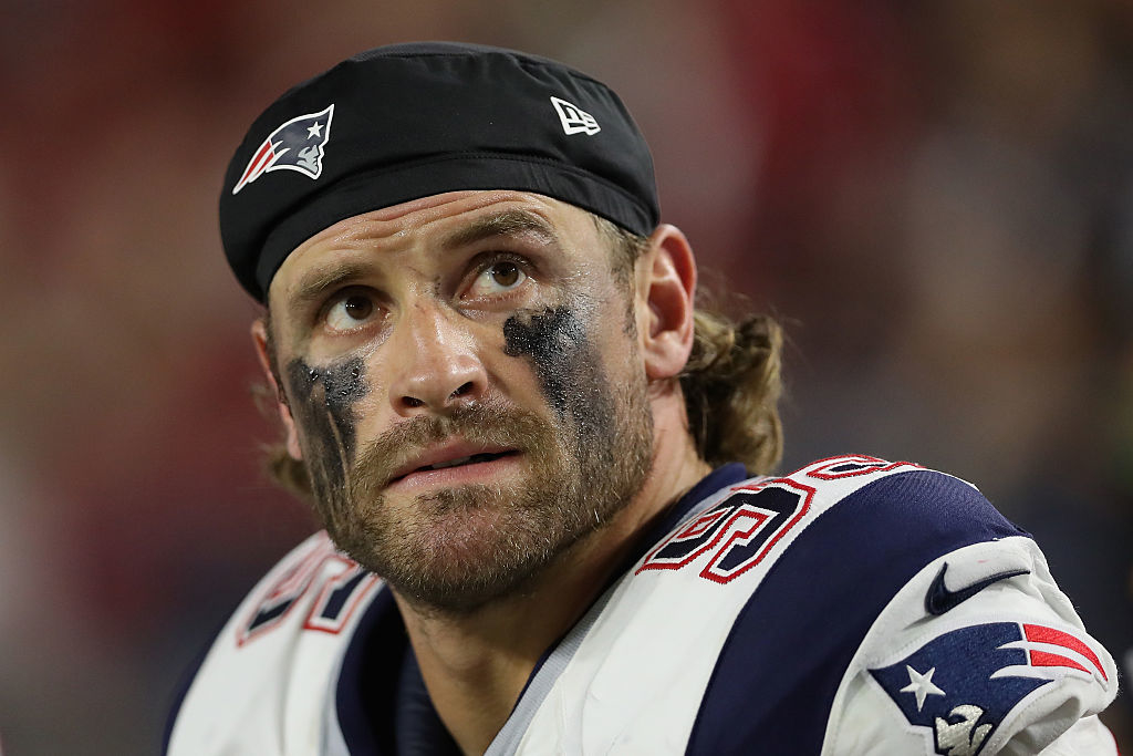 A football player with eye black, wearing a helmet and Patriots jersey featuring the number 50, looking upwards during a game