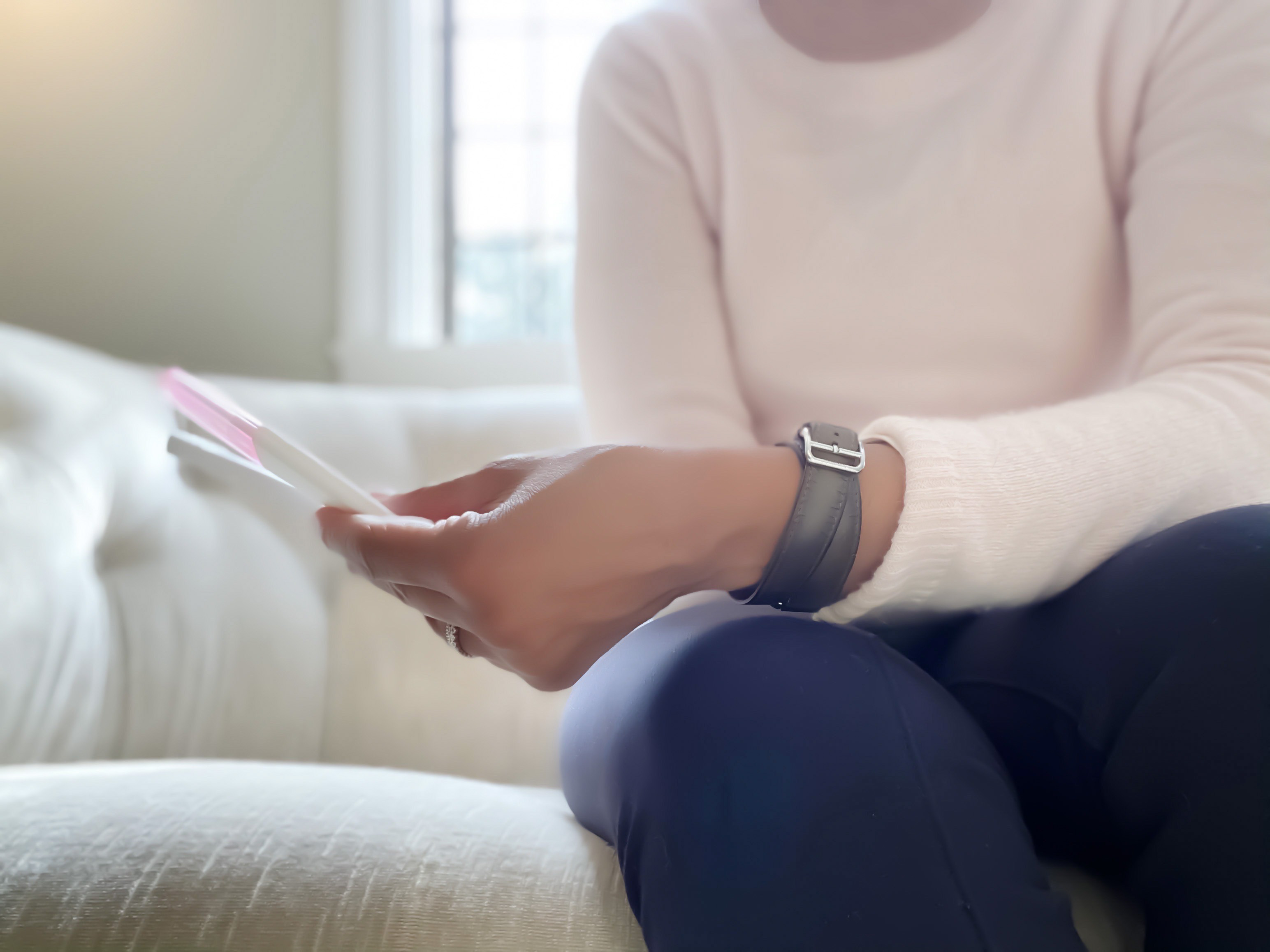 A person wearing a long-sleeve shirt and a watch sits on a couch, holding and looking at papers. The person's face is not visible