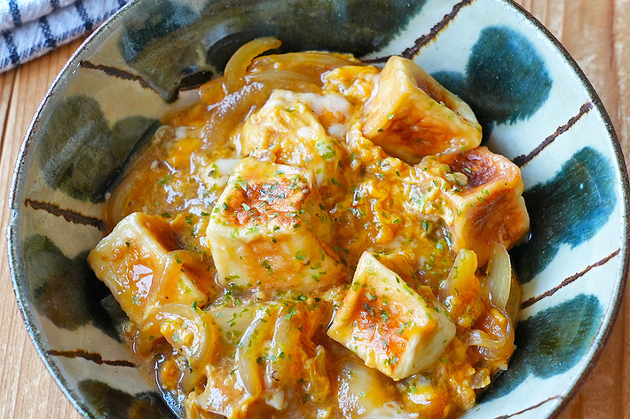 陶器の器に入った美味しそうな麻婆豆腐が木製テーブルに置かれています。上にはネギが散らされています。