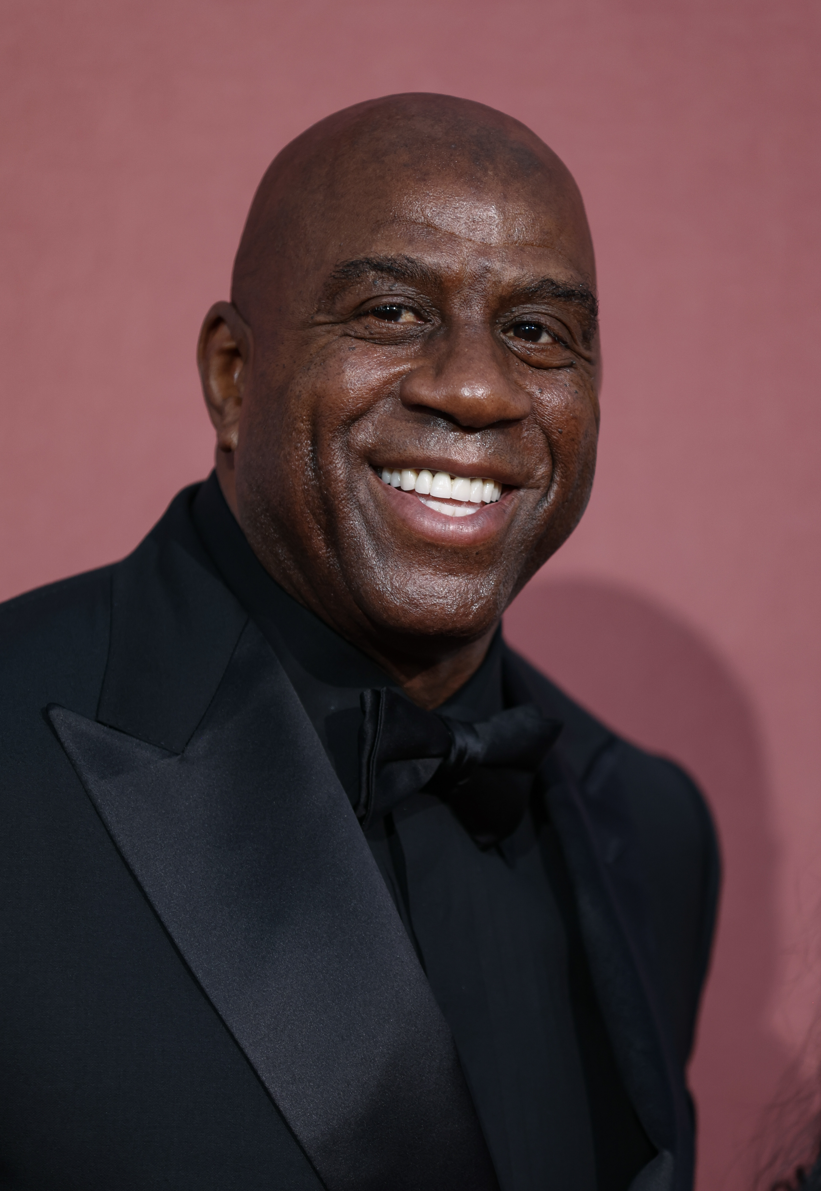 Magic Johnson smiling in a suit with a bow tie at a red carpet event
