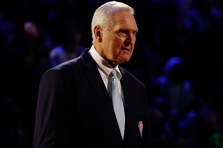 Jerry West in a suit with a light tie, standing in an indoor setting