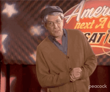 The person in the image is dressed as an elderly man in a cardigan and cap, featured on a stage with "America's Next A" partially visible in the background