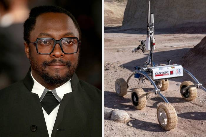 Will.I.Am in a black suit and white shirt next to a Mars rover prototype in a barren landscape