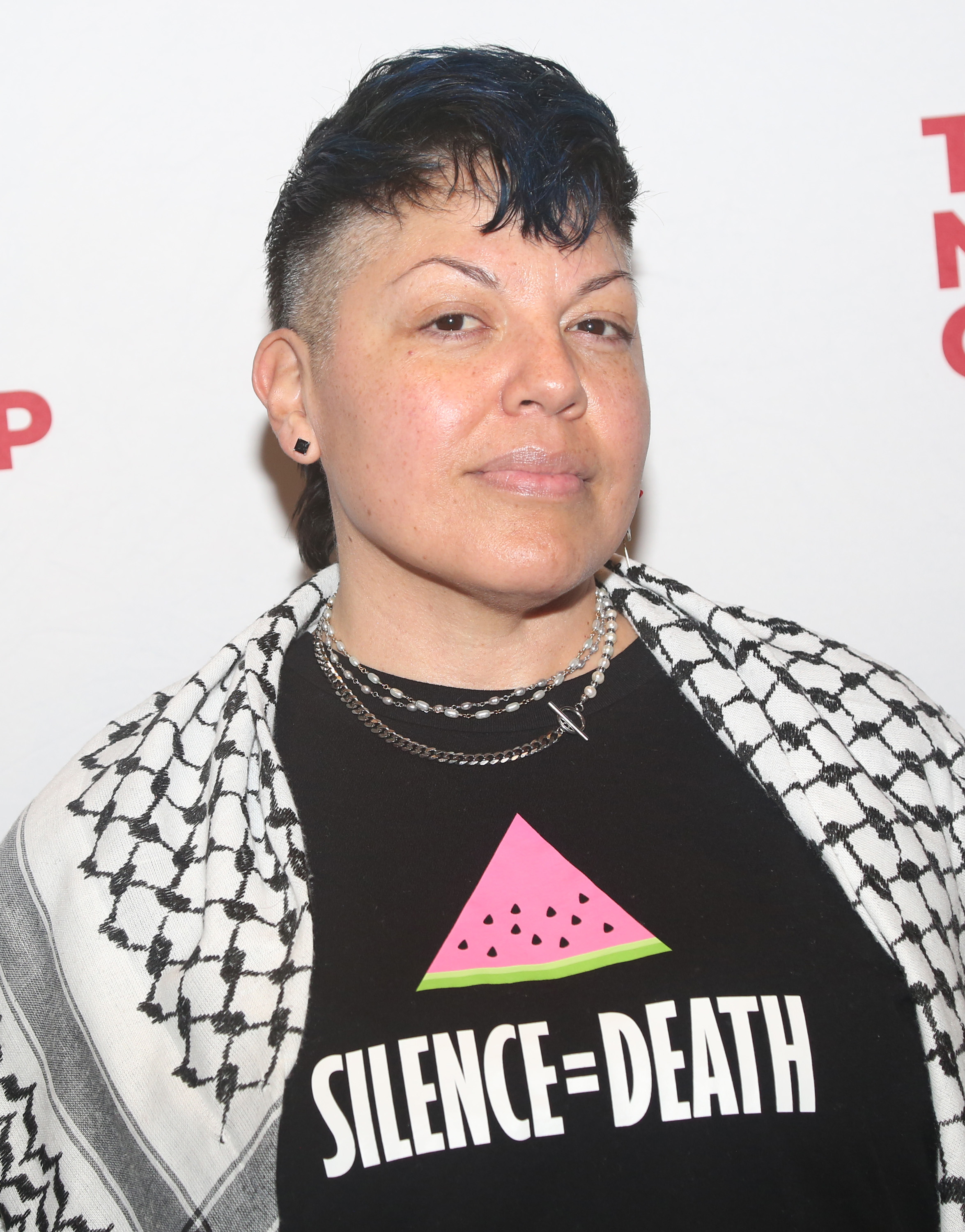 Sara Ramirez at an event wearing a graphic T-shirt that reads &quot;Silence=Death&quot; with a watermelon slice above the text, and a black-and-white patterned shawl