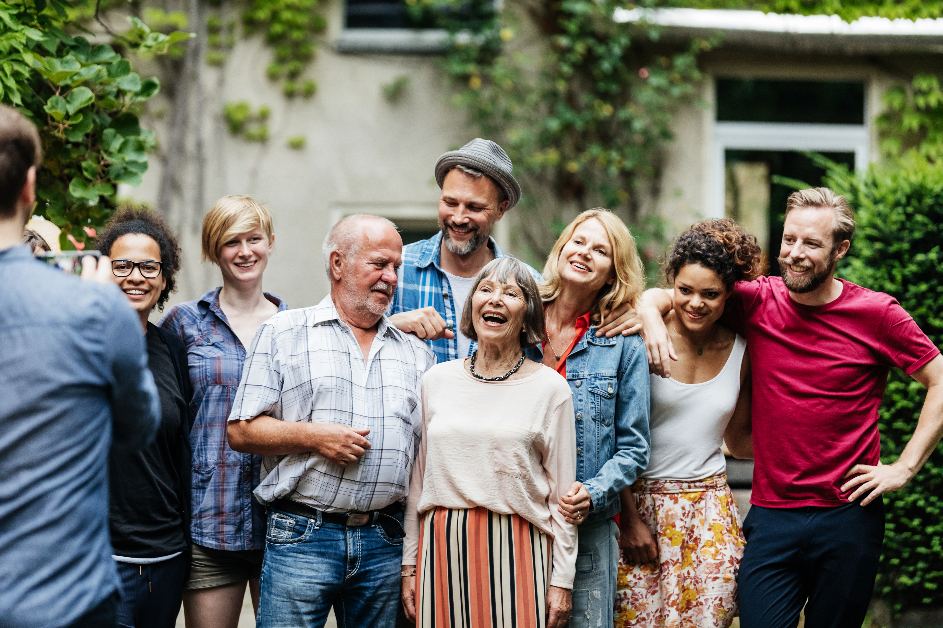 A group of eight people, including an elderly woman, posing together outdoors. They are casually dressed and appear happy and relaxed
