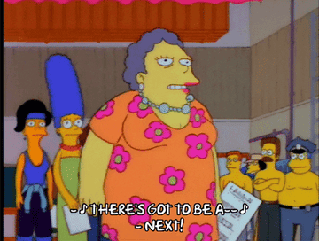 Characters from The Simpsons are in line for auditions. Selma, in a flower dress, holds a paper and sings, while Marge, behind her, watches with others