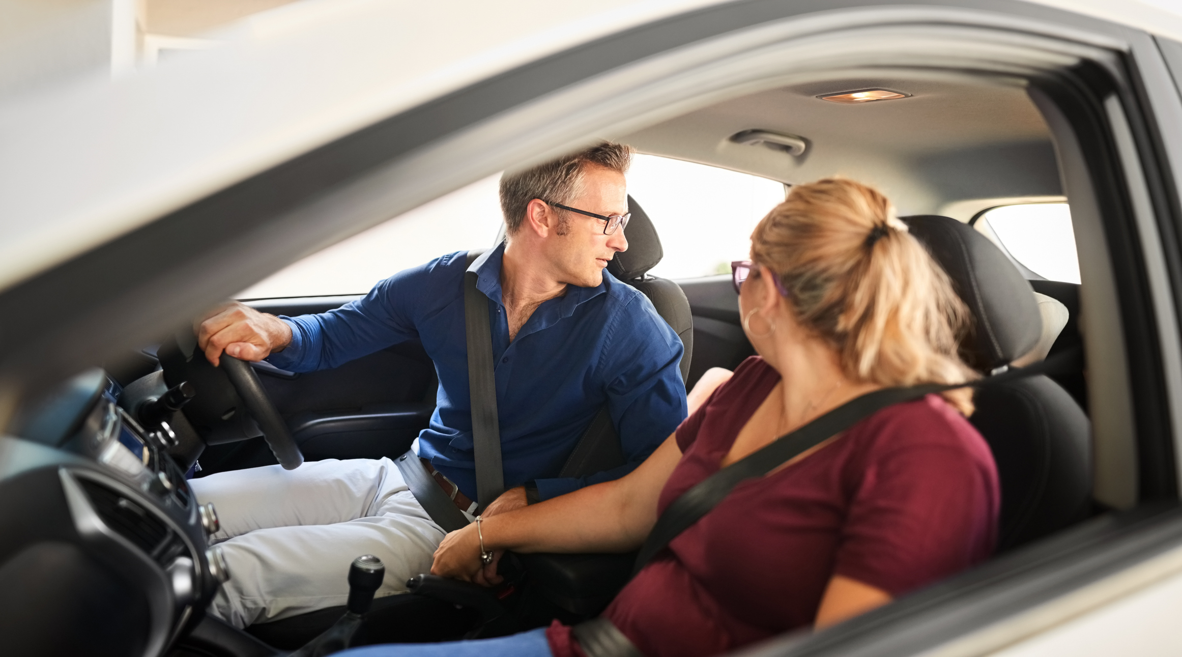 A man and a woman sitting in a car. The man is in the driver's seat looking back, while the woman in the passenger seat looks at him