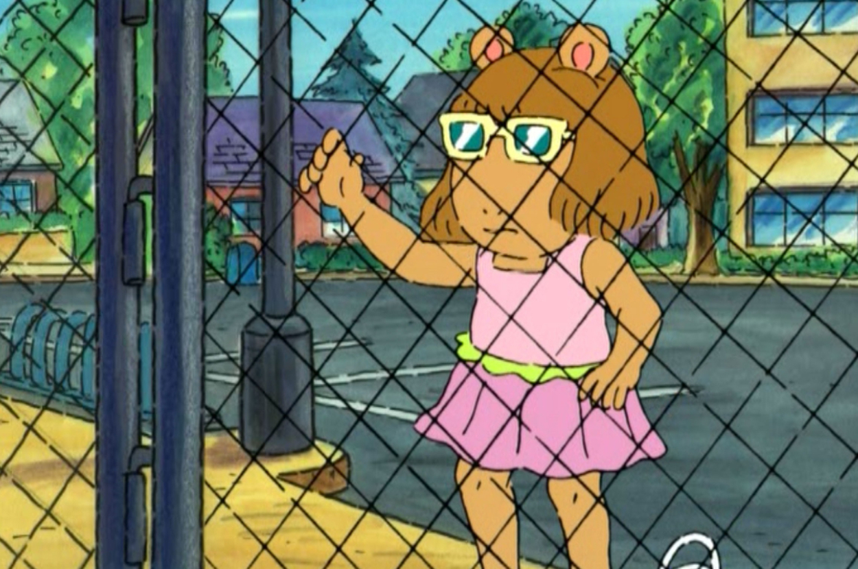 D.W. from Arthur, an animated character, stands behind a chain-link fence, looking through it while wearing a pink dress and sunglasses