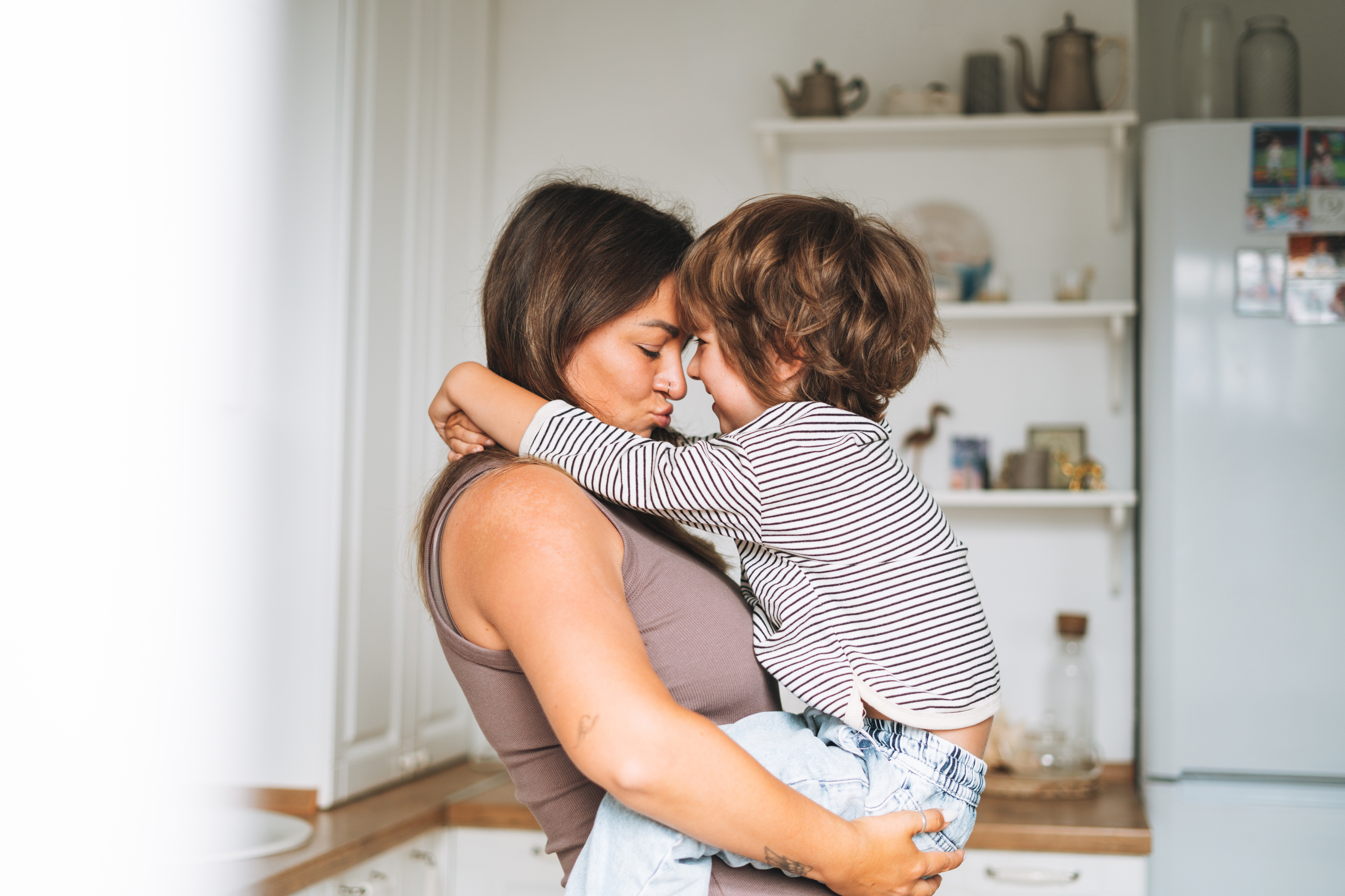 Kim Kardashian holds a child close in a kitchen, both with eyes closed, sharing a tender moment