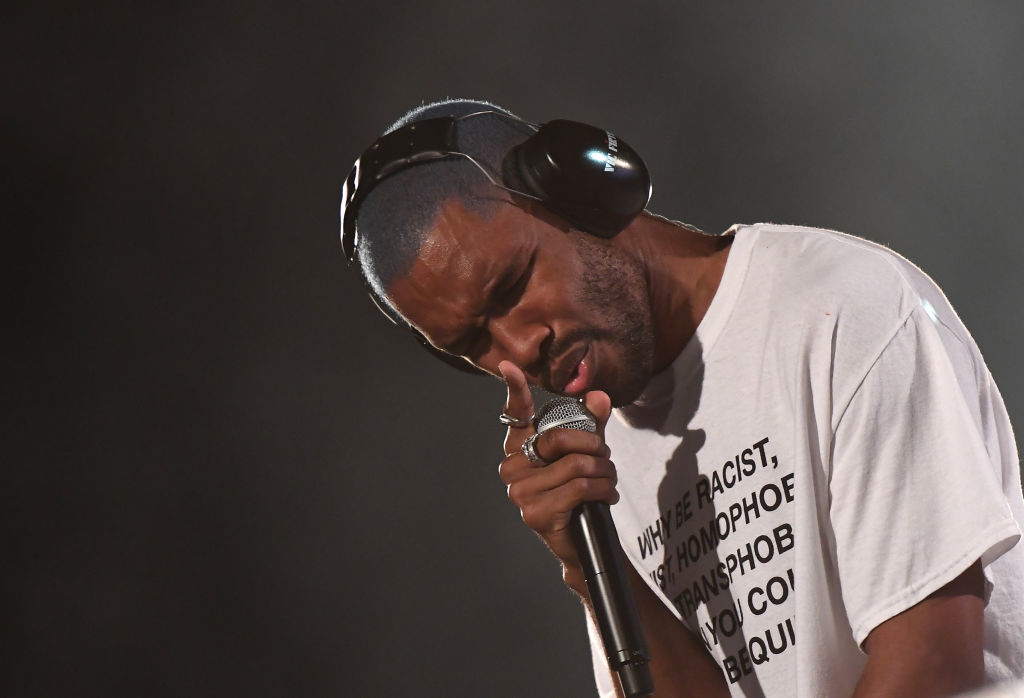 Frank Ocean performing, wearing large headphones and a white T-shirt with text