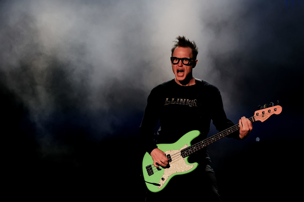 Mark Hoppus of Blink-182 performs energetically on stage while playing a green bass guitar
