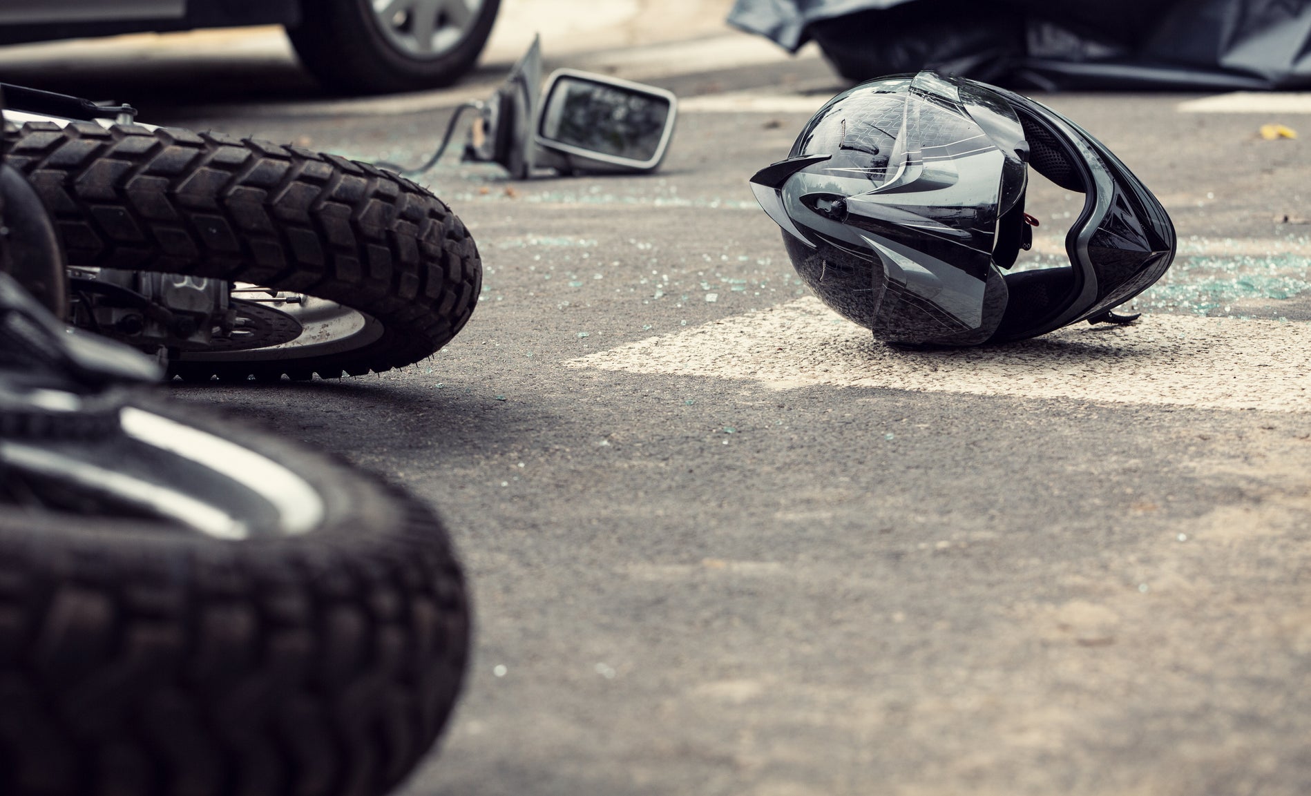 A motorcycle accident with a fallen bike, helmet on the ground, and a damaged car in the background