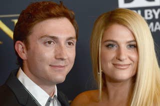 Two people, Daryl Sabara and Meghan Trainor, pose together on a red carpet. Daryl wears a suit jacket. Meghan has long hair styled straight and wears an off-the-shoulder dress