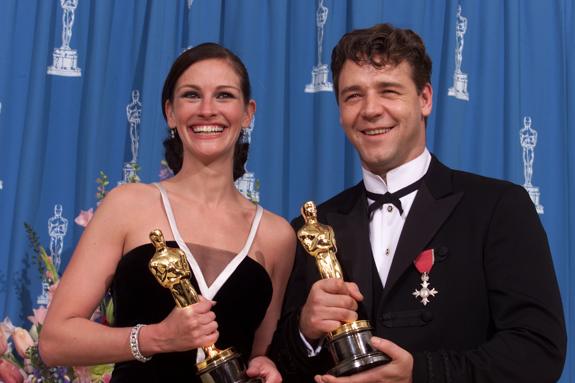 Julia Roberts and Russell Crowe holding Oscars, smiling, and dressed in formal attire at an awards ceremony
