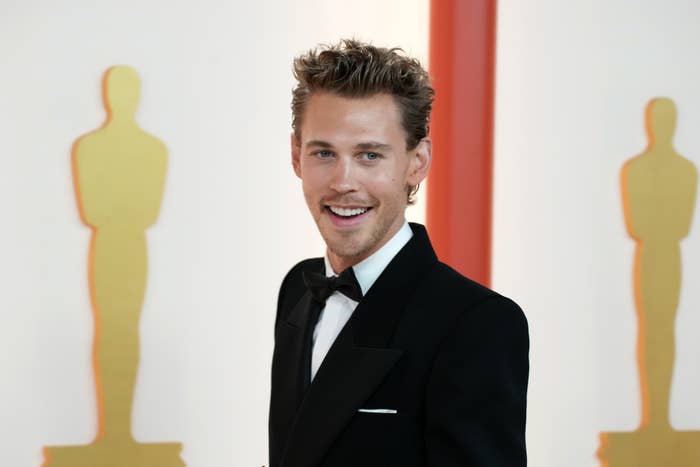 Austin Butler smiles on the red carpet, wearing a classic black tuxedo with a white shirt and black bow tie