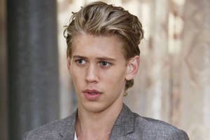 Austin Butler wearing a casual outfit with a gray blazer over a white shirt. He is standing indoors
