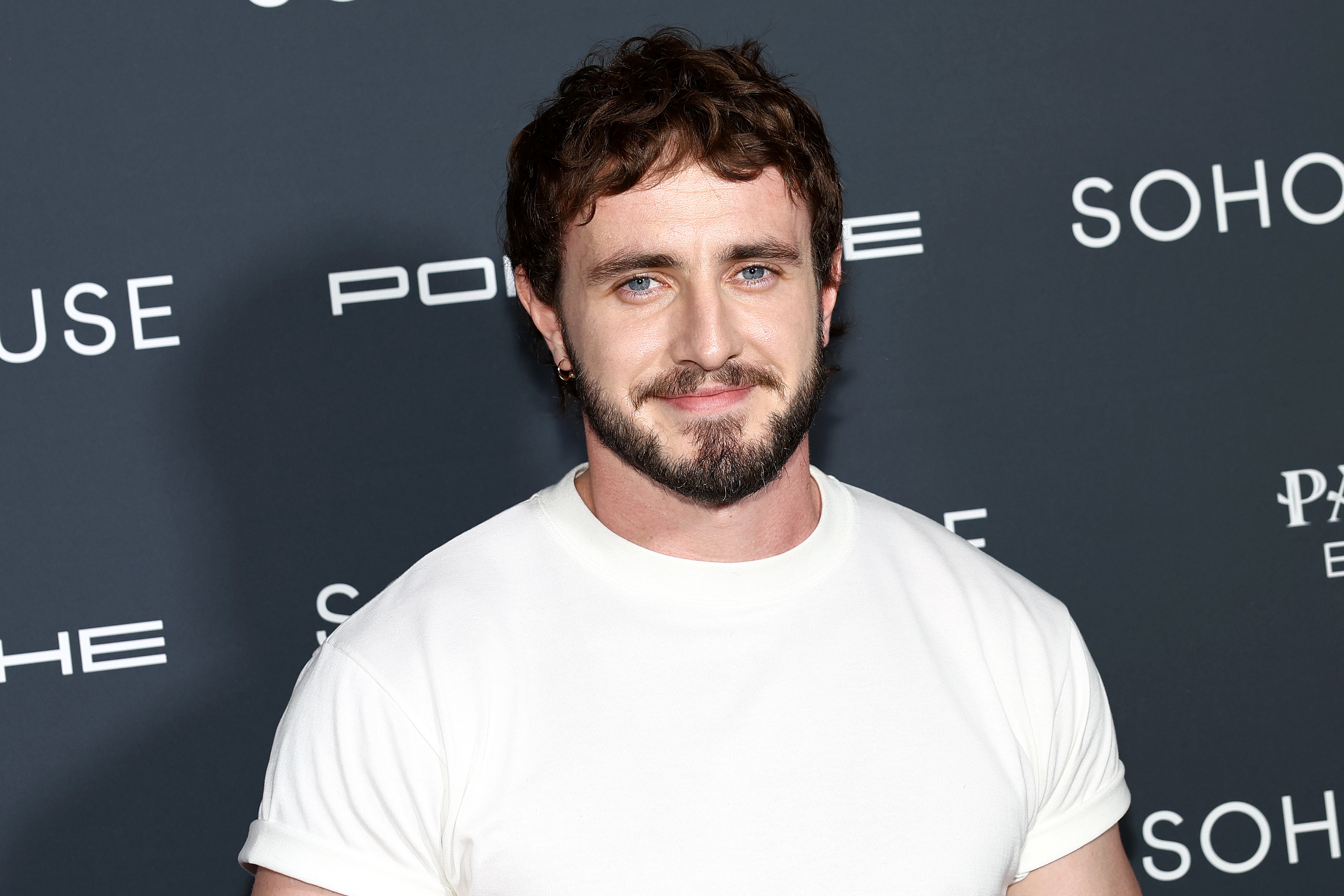 Paul Mescal at a Porsche and Soho House event, wearing a plain white t-shirt and smiling at the camera