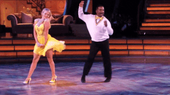 Alfonso Ribeiro and Witney Carson perform an energetic dance routine on a stage. Witney wears a short dress and Alfonso wears a sweater and pants