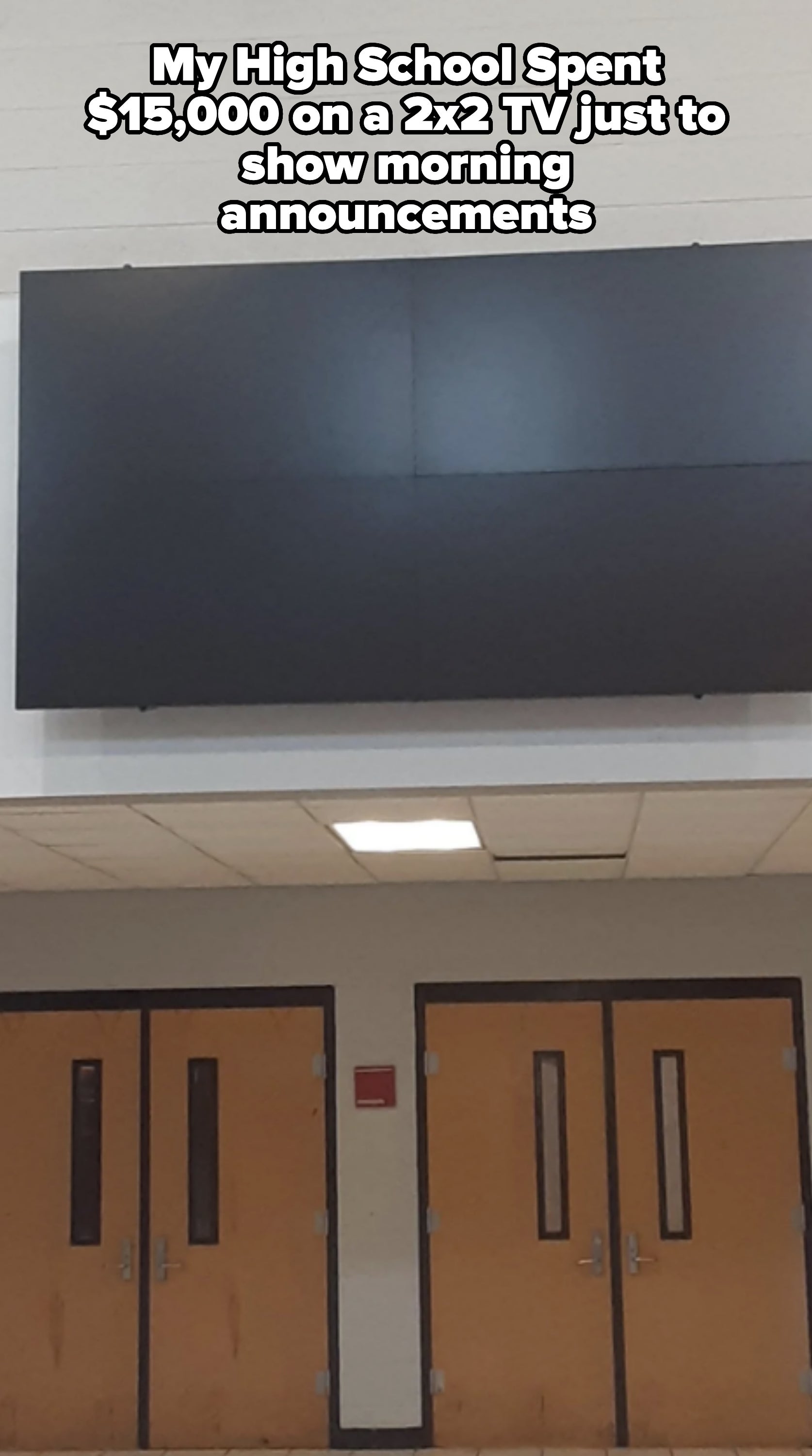 A large blank display screen mounted above a set of double doors in a public building