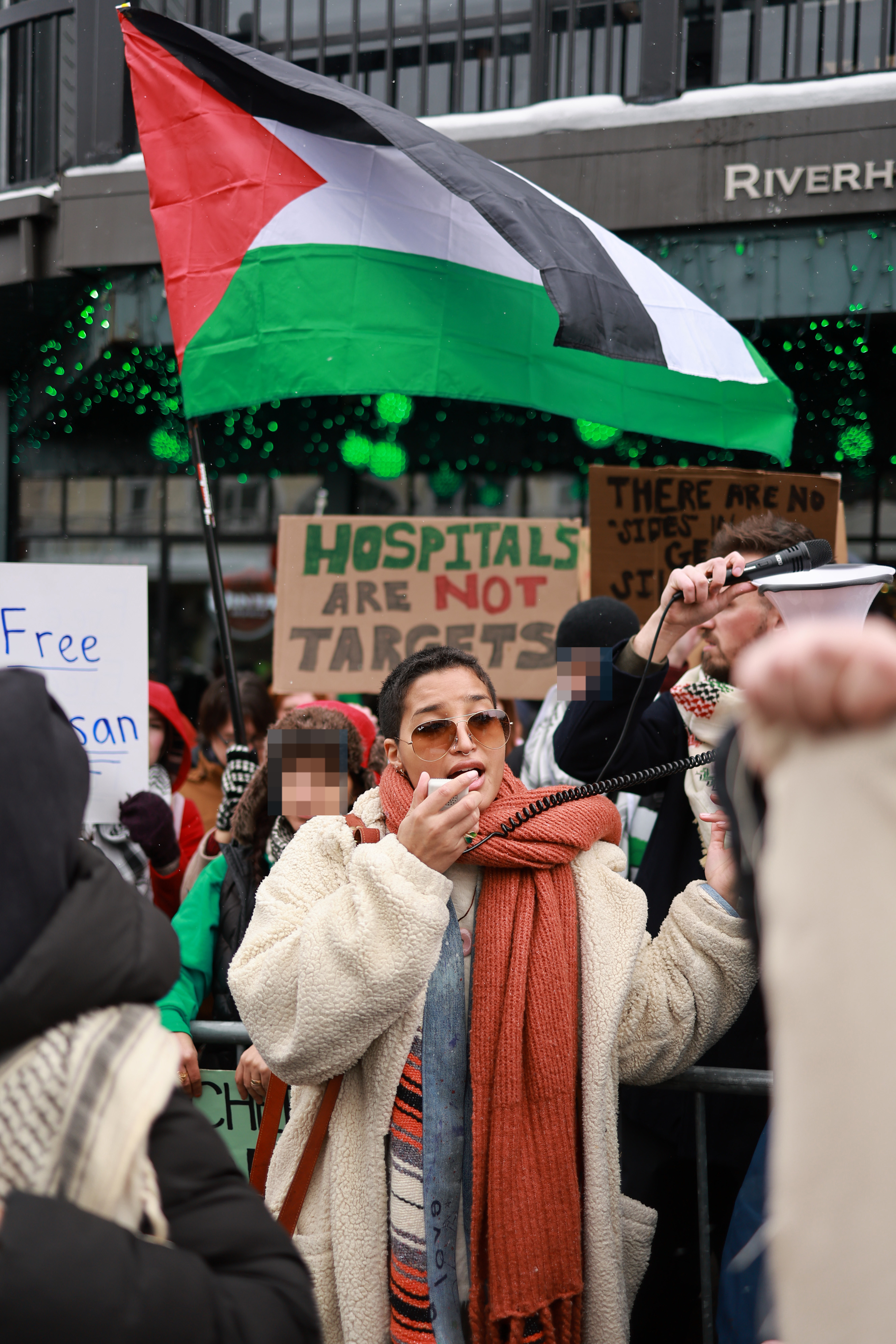 Protestors holding signs and Palestinian flags, with one woman in the front using a megaphone. Signs read, &quot;Free&quot; and &quot;Hospitals Are Not Targets.&quot;