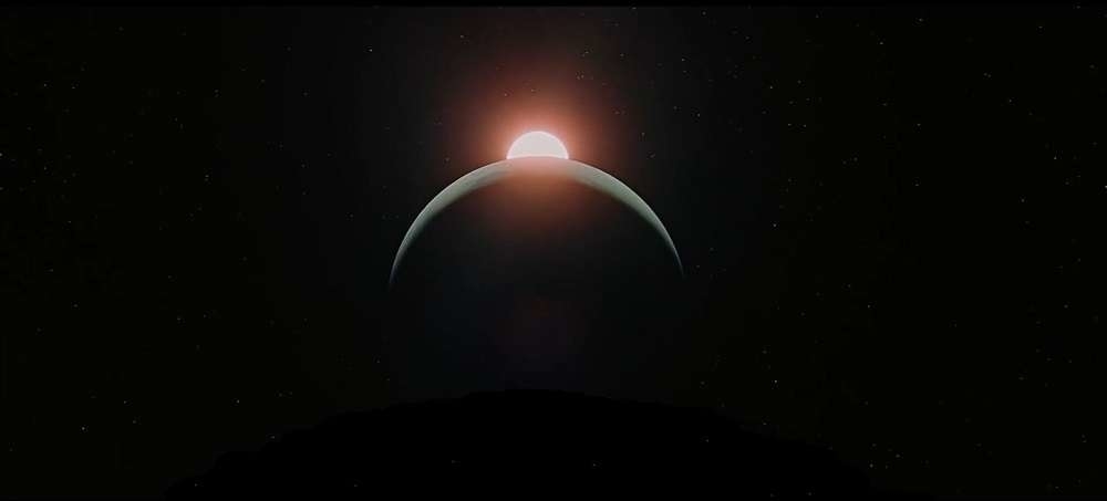 A large planet is partially illuminated by a glowing sun, creating a crescent shape in a star-filled space scene