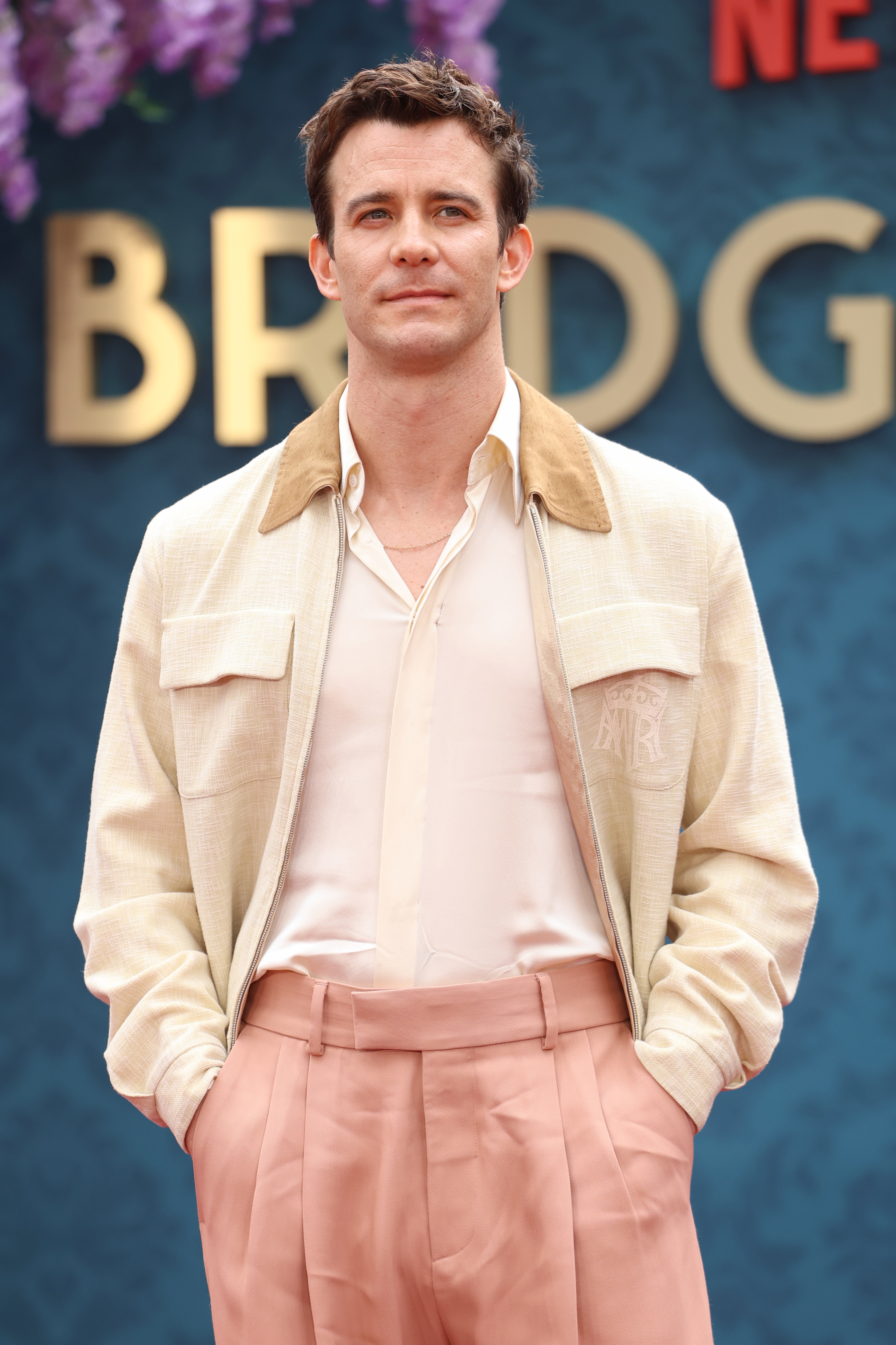 Luke Thompson at a red carpet event, wearing a light jacket, white shirt, and high-waisted trousers