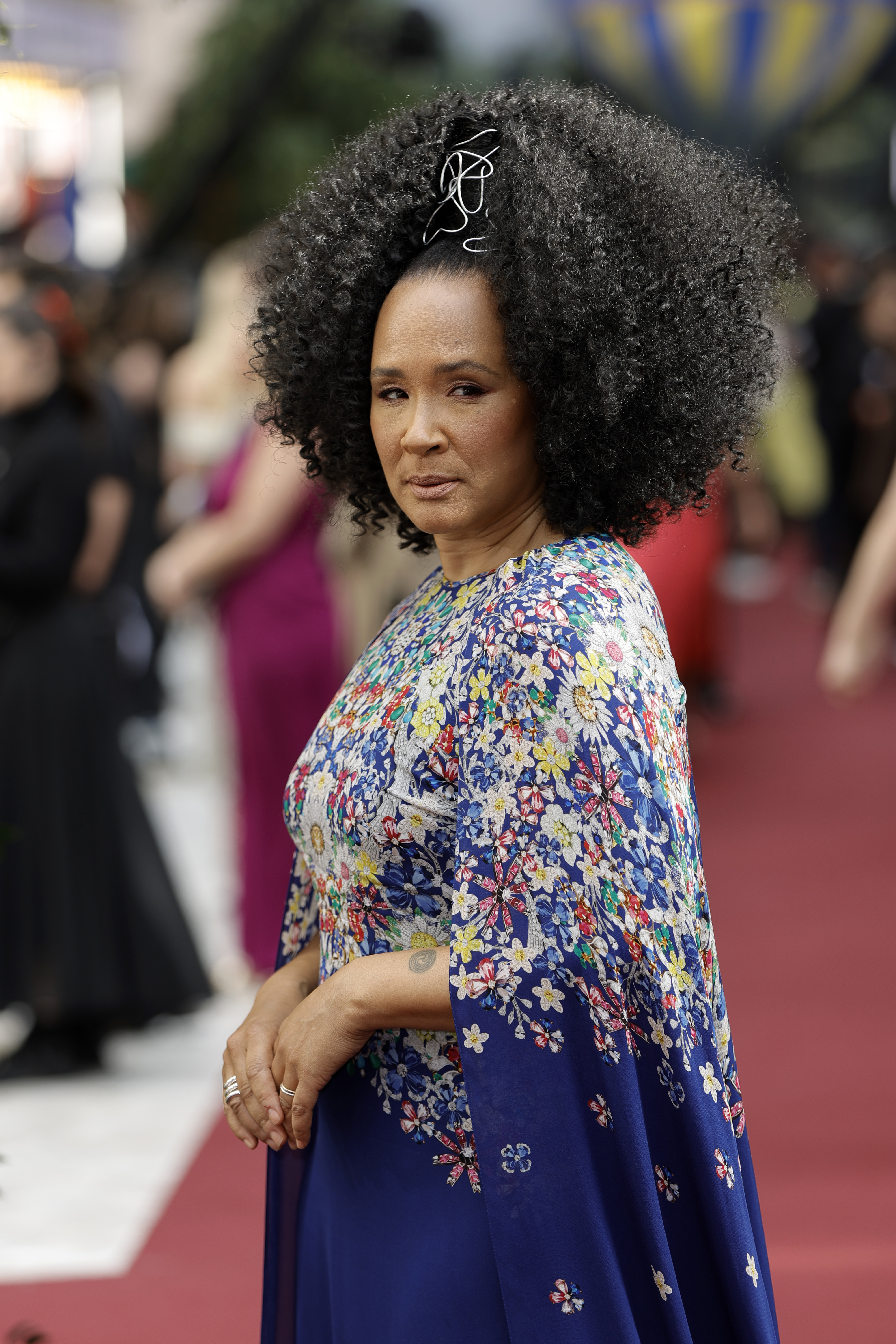Golda Rosheuvel on the red carpet wearing a floral-patterned, floor-length dress with a large, curly hairstyle