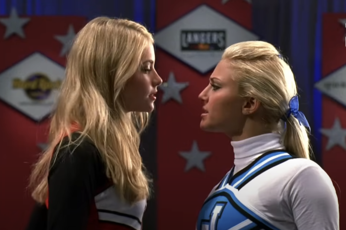 Sierra Capri (left) and Olivia Scott Welch (right) face each other, dressed in cheerleader uniforms, in a tense scene from a TV show or movie