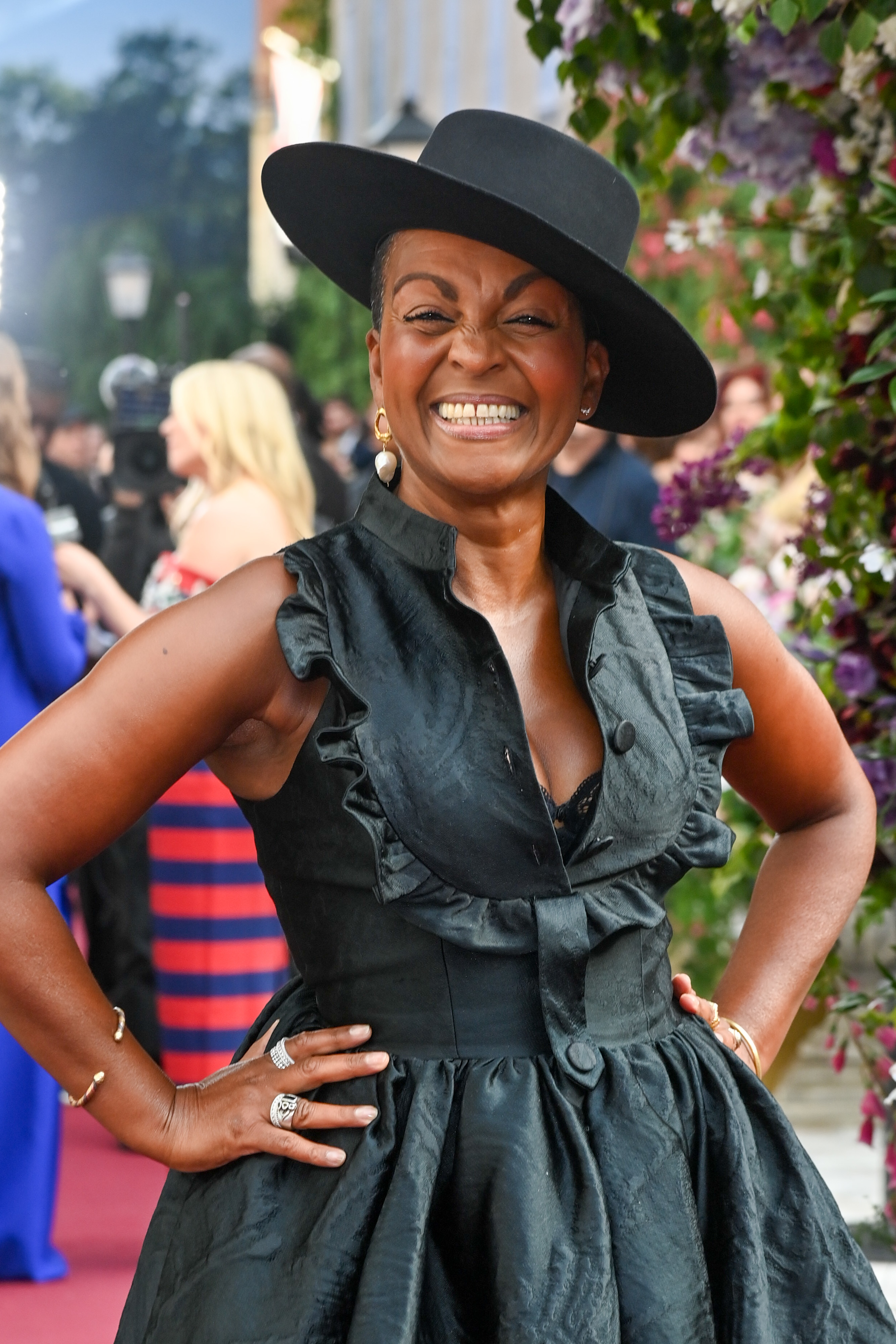 Adjoa Andoh at a red carpet event, smiling widely, wearing a ruffled black dress and a black hat