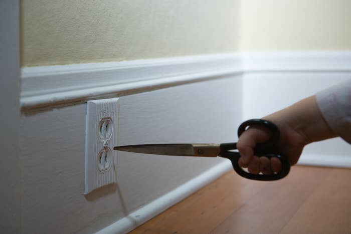 A small child's hand is holding a pair of scissors very close to an electrical outlet, posing a dangerous situation