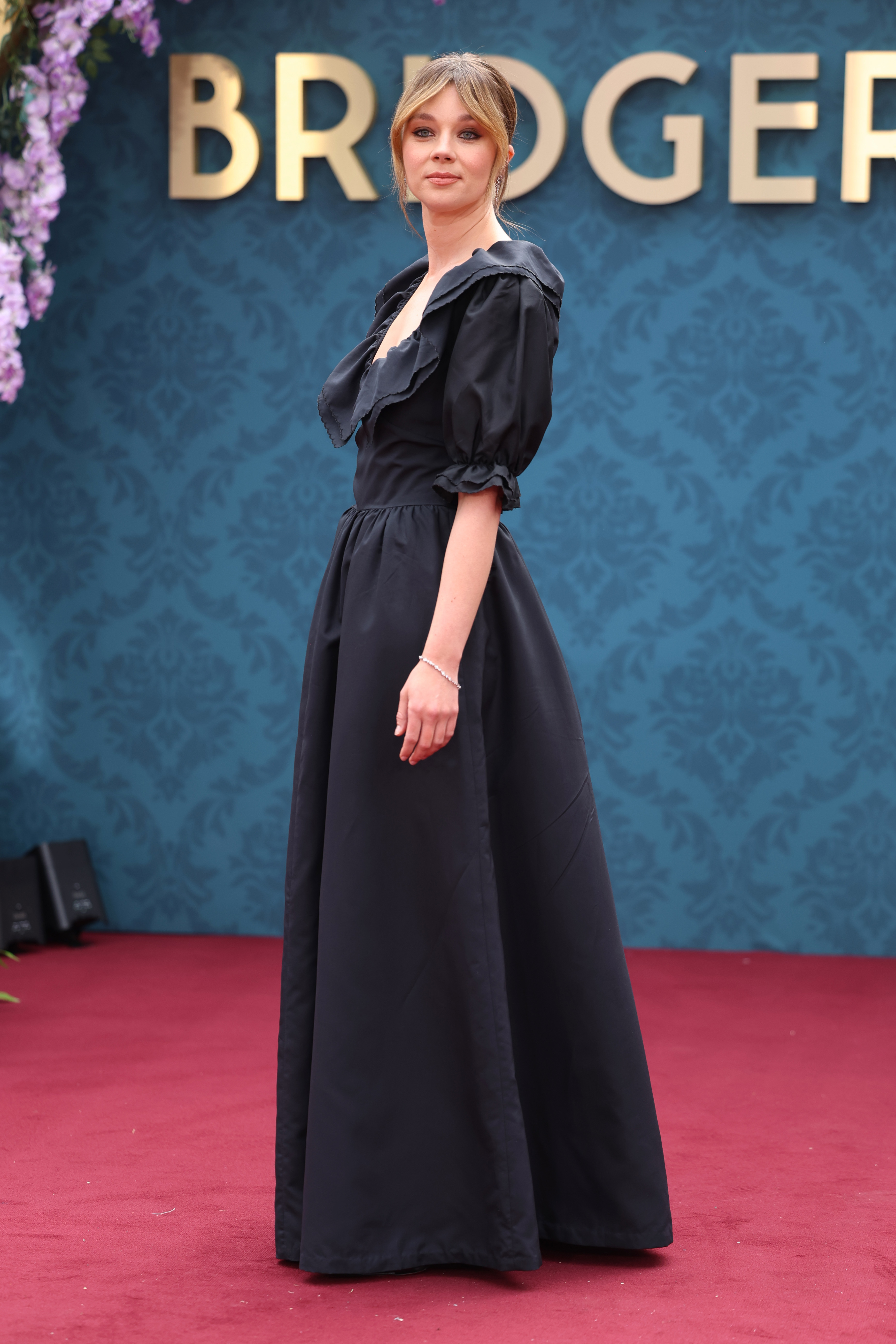 Claudia Jessie in an elegant, floor-length dark dress at a 'Bridgerton' event on a red carpet