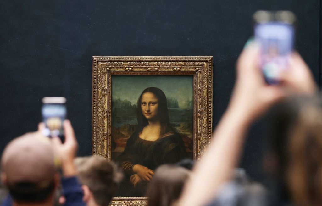 The image shows the Mona Lisa painting by Leonardo da Vinci in a museum, with visitors photographing it