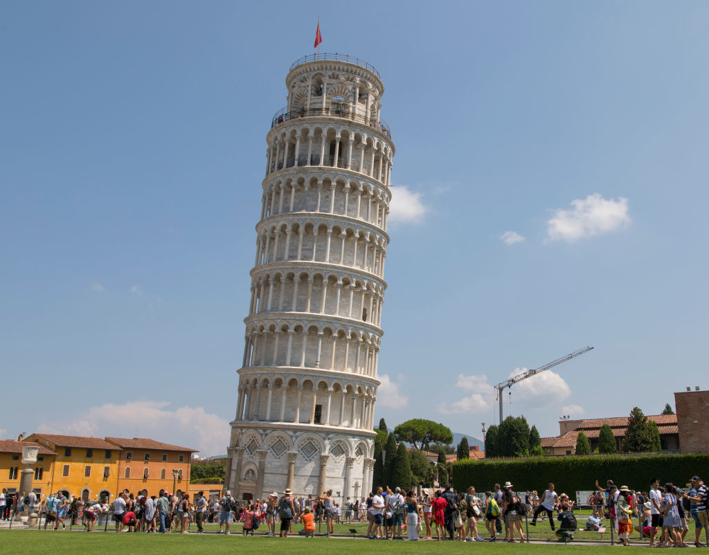 The Leaning Tower of Pisa with many tourists gathered around the base, some taking photos and enjoying the clear day