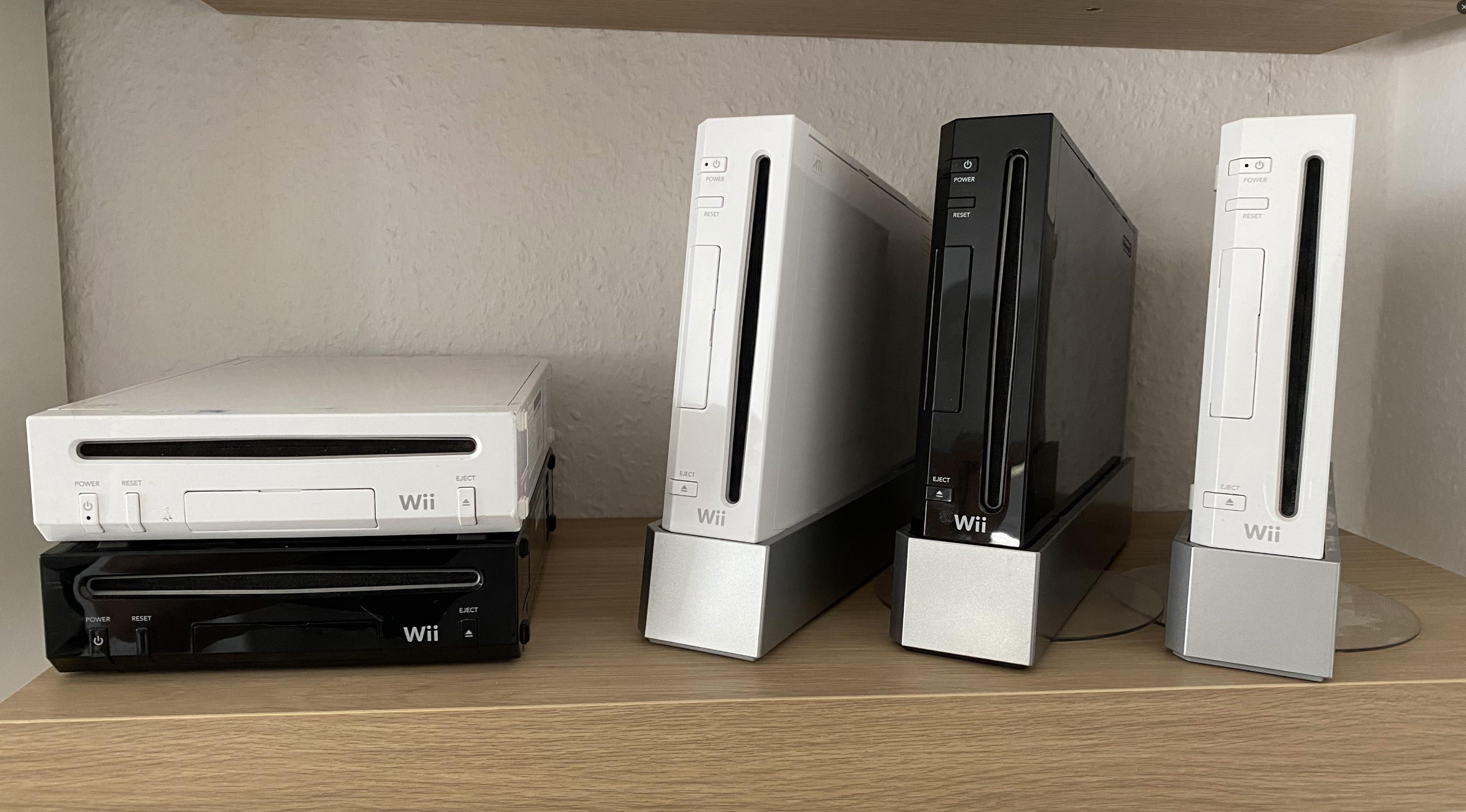 A shelf displaying five Nintendo Wii consoles in various orientations and colors