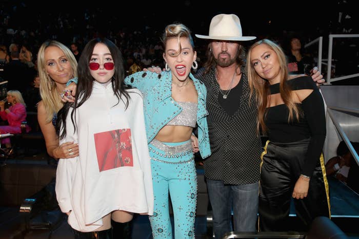 Tish Cyrus, Noah Cyrus, Miley Cyrus, Billy Ray Cyrus, and Brandi Cyrus pose together. Miley wears a turquoise studded outfit, Noah wears a white oversized sweatshirt